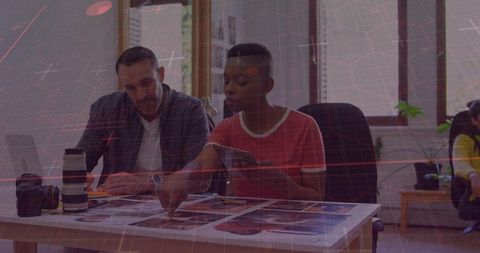 Creative team collaborating over layout prints and tablet in modern design studio workspace