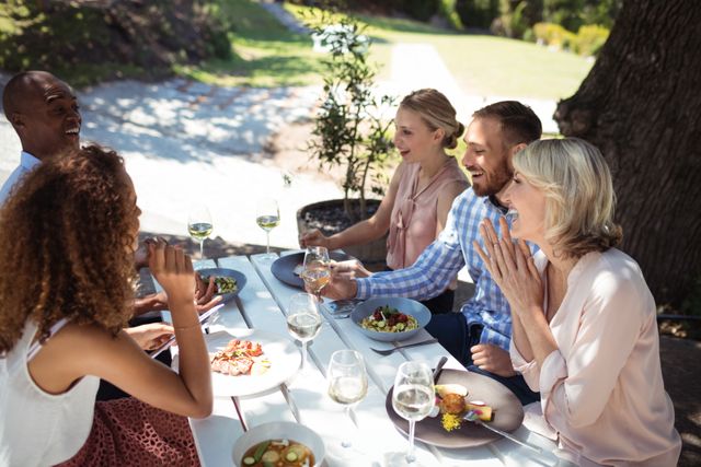 Group of friends enjoying a meal together outdoors, engaging in lively conversation and laughter. Ideal for use in advertisements for restaurants, social gatherings, and lifestyle blogs promoting friendship and leisure activities.