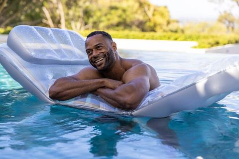 Mature african american man relaxing on inflatable lounger in sunny backyard pool