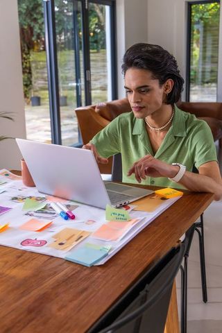 Asian man working on laptop at home workspace with colorful sticky notes and planning