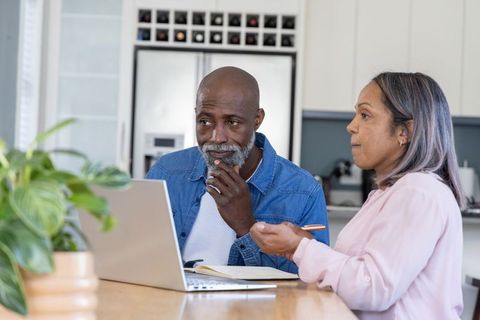 Mature Black Couple Reviewing Finances on Laptop at Modern Kitchen Island, Budgeting