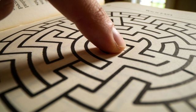 Tracing fingertip through printed circular maze on open book page, closeup puzzle