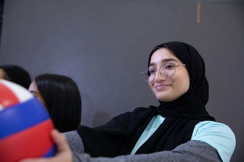 Muslim woman in hijab and glasses holding tricolor volleyball, teamwork and confidence