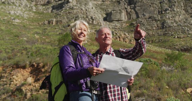 Senior couple enjoying a hike in mountainous terrain while consulting a paper map. Ideal for content related to active aging, outdoor activities, travel, retirement lifestyle, and adventure planning.