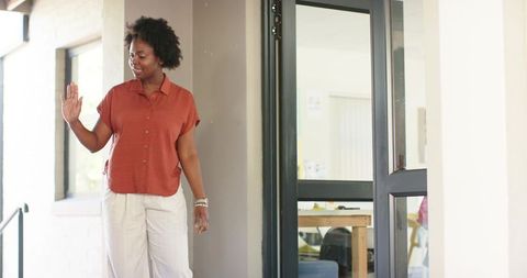 African american woman waving at office entrance by glass door with modern workspace
