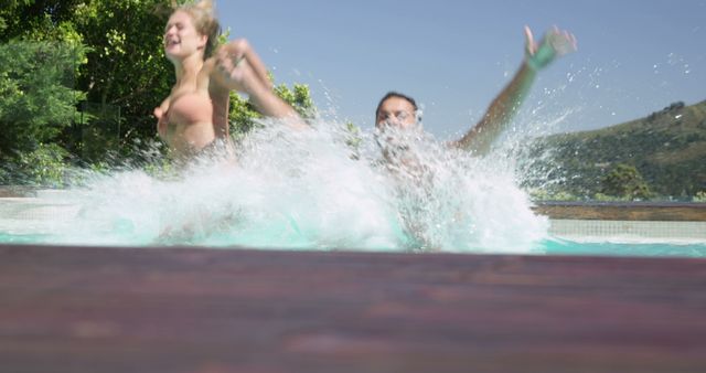 Two friends are seen joyfully jumping into a pool, creating a large splash in the water. The image exudes summer fun and excitement, perfect for themes related to holidays, leisure activities, and outdoor enjoyment. It can be used in promotional materials for pool parties, summer events, travel brochures, or advertisements for swimwear and recreational products.