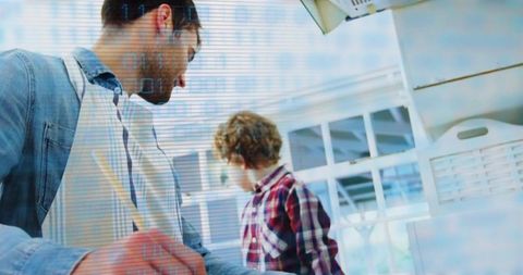 Father stirring at kitchen counter while son watching through window, family cooking lifestyle