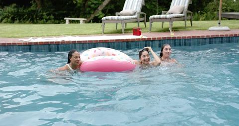 Multicultural women enjoying backyard pool party with pink donut float and red cooler