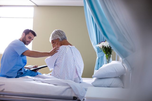 Male doctor consoling a senior patient on bed in hospital