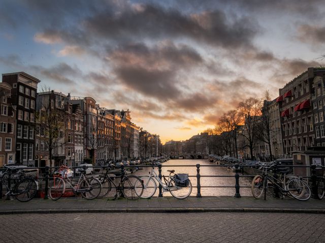 Bicycles lined ornamentally on Amsterdam canal bridge during serene sunset - Download Free Stock Photos Pikwizard.com