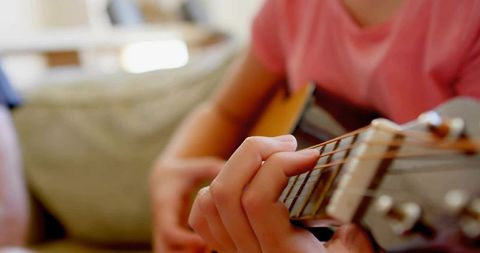 Child Practicing Acoustic Guitar with Focus on Strings at Home