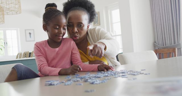 Happy african american granddaughter and grandmother doing jigsaw puzzle at home, copy space. Science, education, learning, family and domestic life.