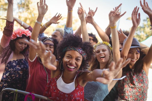 Group of friends celebrating at an outdoor music festival, dancing and smiling with hands raised. Perfect for use in advertisements, social media posts, and articles related to music festivals, summer events, youth culture, and group activities.