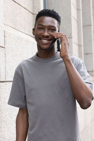 Smiling african man talking on smartphone outdoors by urban stone wall casual portrait