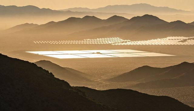 Golden desert solar field reflecting low sun with mirrored heliostats and tower silhouette