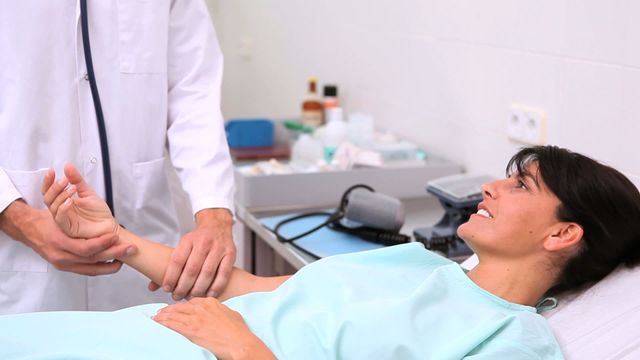 This video shows a doctor taking the pulse of a female patient lying in a hospital bed. It depicts a medical professional conducting a routine checkup or examination. The background features medical equipment and supplies that highlight the healthcare setting. This can be used for medical presentations, healthcare advertising, informative brochures on hospital care, or articles about the patient-doctor relationship.