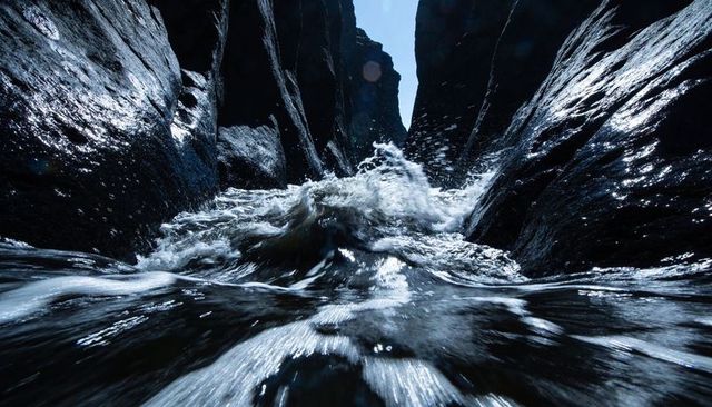 Surging wave crashing between jagged wet rock walls at water level with foamy spray