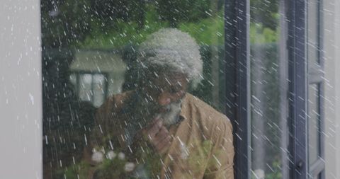 Contemplative elder behind rain-soaked window
