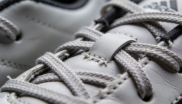 Macro close-up gray sneaker laces showing braided texture, keeper and leather grain