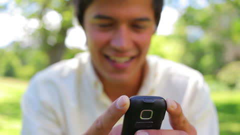 Smiling Man Typing on Old Mobile Phone in Nature