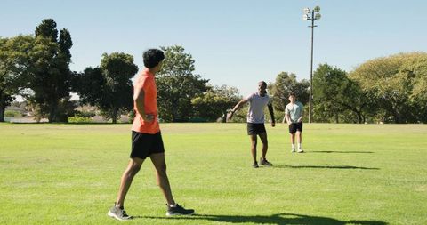 Three men stretching on park sports field preparing for outdoor workout