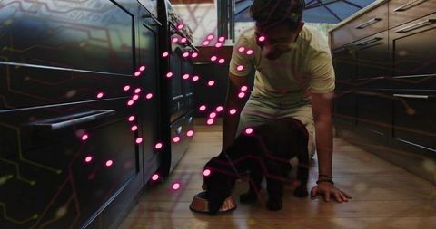 Asian Man Kneeling Feeding Black Dog in Modern Kitchen with Pink Digital Tech Overlay