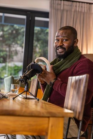 African american man podcasting from cozy home studio holding headphones and speaking