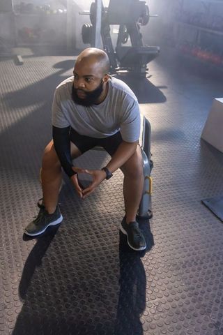 African american man resting on gym bench, clasping hands and wearing fitness watch