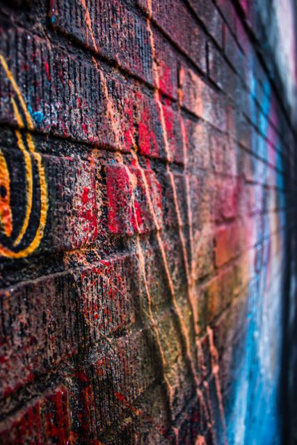 Close-up of a brick wall covered with vibrant and colorful graffiti. The diverse colors and textures create a dynamic and edgy urban feel. This image is suitable for use in design projects, art-related content, blogs about street culture, and marketing materials that focus on urban trends and gritty aesthetics.