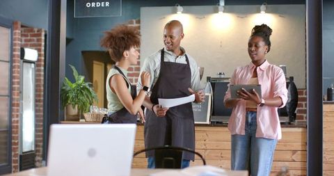 African american barista team collaborating behind wooden coffee counter using tablet