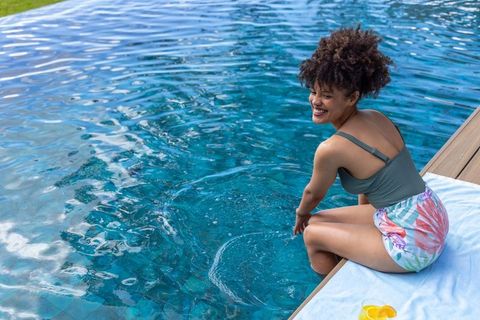 African american woman relaxing at pool edge in green swimsuit and tropical sarong