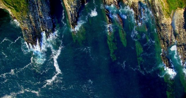 Aerial view of rugged cliffs meeting the ocean, showcasing the dynamic interaction between land and water. The image captures the natural beauty and power of coastal landscapes.