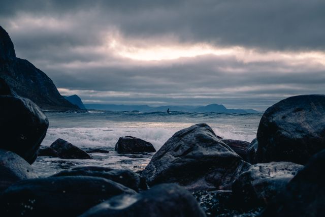 Beautiful coastal scene featuring a rocky beach at dusk, under an overcast sky. Waves gently crash against the rocks, giving the scene a dramatic and moody atmosphere. Ideal for use in articles about coastal environments, travel inspiration, nature photography, or scenic wallpapers.