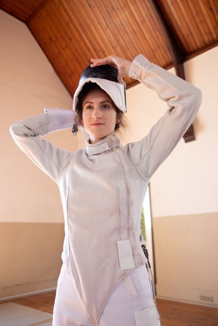 Caucasian woman wearing protective fencing clothes, putting on a mask, in a gym. Sport and working out.