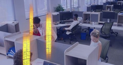 Diverse team collaborating in open office with workstations, monitors and warm lighting