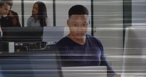 African American man typing at multi-monitor workstation in open-plan office collaborating