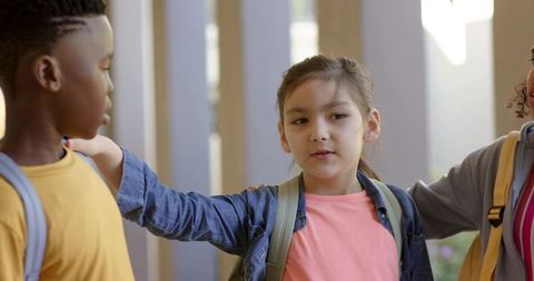 Diverse elementary classmates sharing supportive moment in school corridor with backpacks