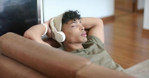 Young man relaxing on couch wearing headphones and beanie, minimalist home lounge