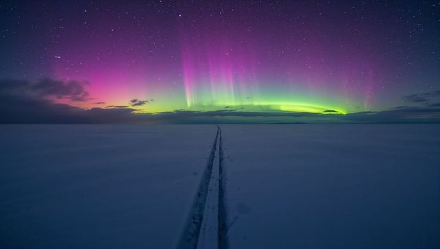 Aurora borealis casting colorful light over frozen plain with parallel tracks to horizon