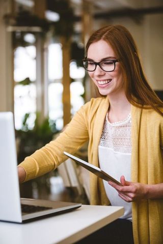 Young Professional Woman Working on Laptop With Tablet in Modern Office