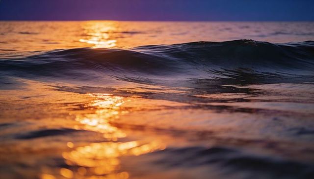 Golden sunset reflecting on rolling ocean wave crest near horizon at twilight