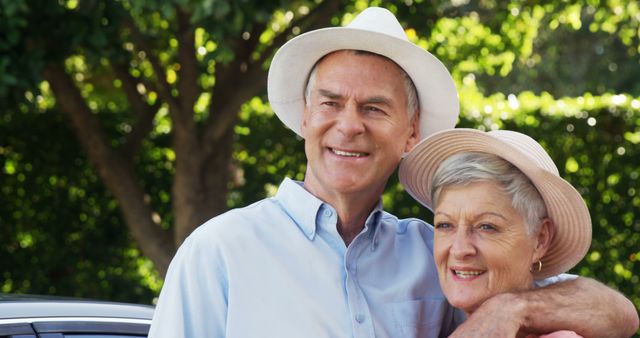 A senior Caucasian couple smiles warmly, standing outdoors with greenery in the background, with copy space. Their affectionate pose and joyful expressions convey a sense of companionship and contentment in their golden years.