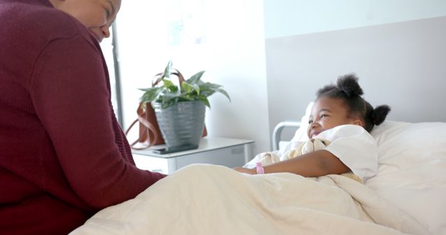 Mother sits by hospital bed visiting young daughter who is resting. Suitable for topics on healthcare, family support, pediatric care, hospital visits, and patient recovery. Useful for healthcare websites, family health articles, and medical brochures.