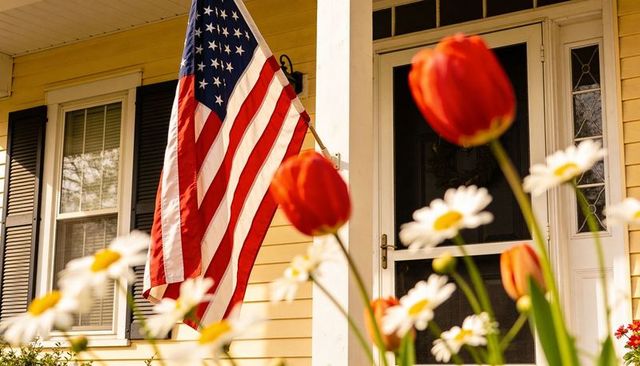 Waving american flag on sunny yellow porch with red tulips and white daisies