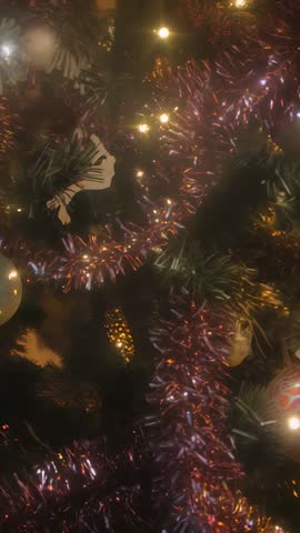 Vertical drifting over Christmas tree branch with purple tinsel and warm glowing lights