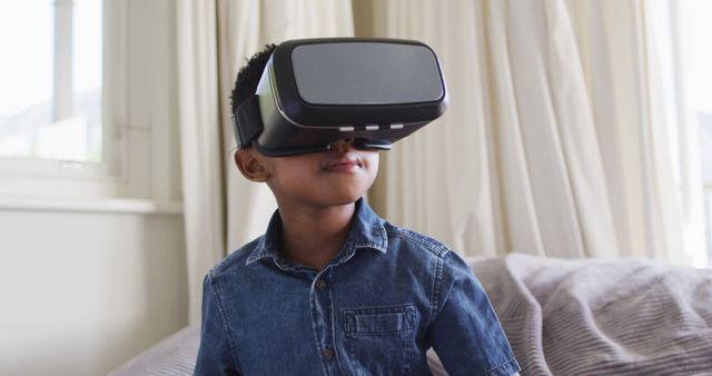 A young boy is exploring a virtual environment using a VR headset in his living room. This image can be used to illustrate topics in technology, modern lifestyle, child development, education, and gaming enthusiasm. Suitable for blogs, articles, and promotional material related to virtual reality and its impact on children.