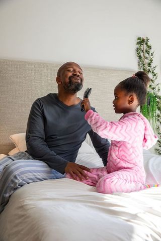 Little girl brushing father's beard on bed during cozy morning bonding in pajamas