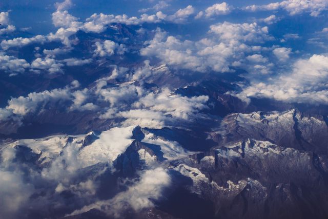 Aerial view of snow-capped mountains partially covered with clouds, showcasing the beauty of nature from above. Perfect for travel brochures, nature photography collections, adventure marketing materials, and websites promoting outdoor activities.