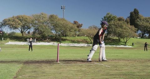 Female Cricket Player Preparing to Bat on Field in Sunny Day