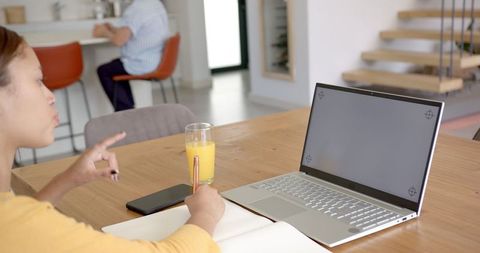 Woman Writing in Notebook with Laptop and Juice at Home